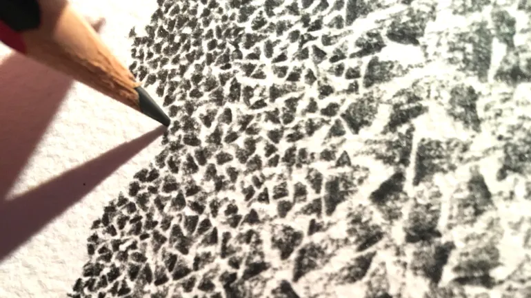 Mine d'un crayon à papier griffonnant sur feuille blanche cartonnée.