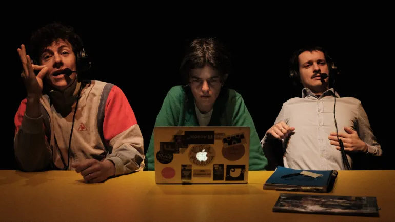 Trois comédiens attablés, portent un casque sur les oreilles avec un micro et un ordinateur.