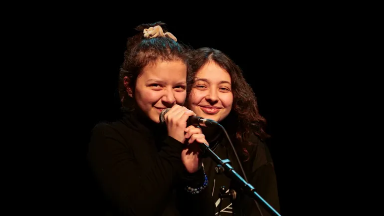 Portrait de deux jeunes femmes souriantes, face caméra, derrière un micro.