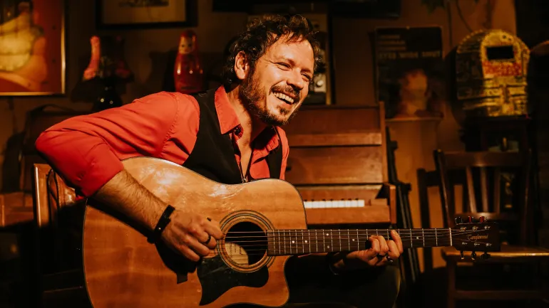 Portrait du musicien Gil, souriant et jouant de la guitare.