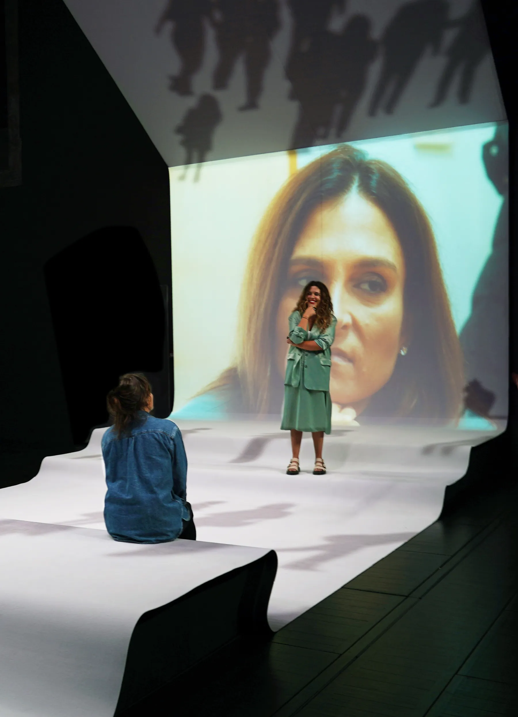 Décor du spectacle Affaires Familiales, tapis et écran blanc, deux comédiennes se parlent.