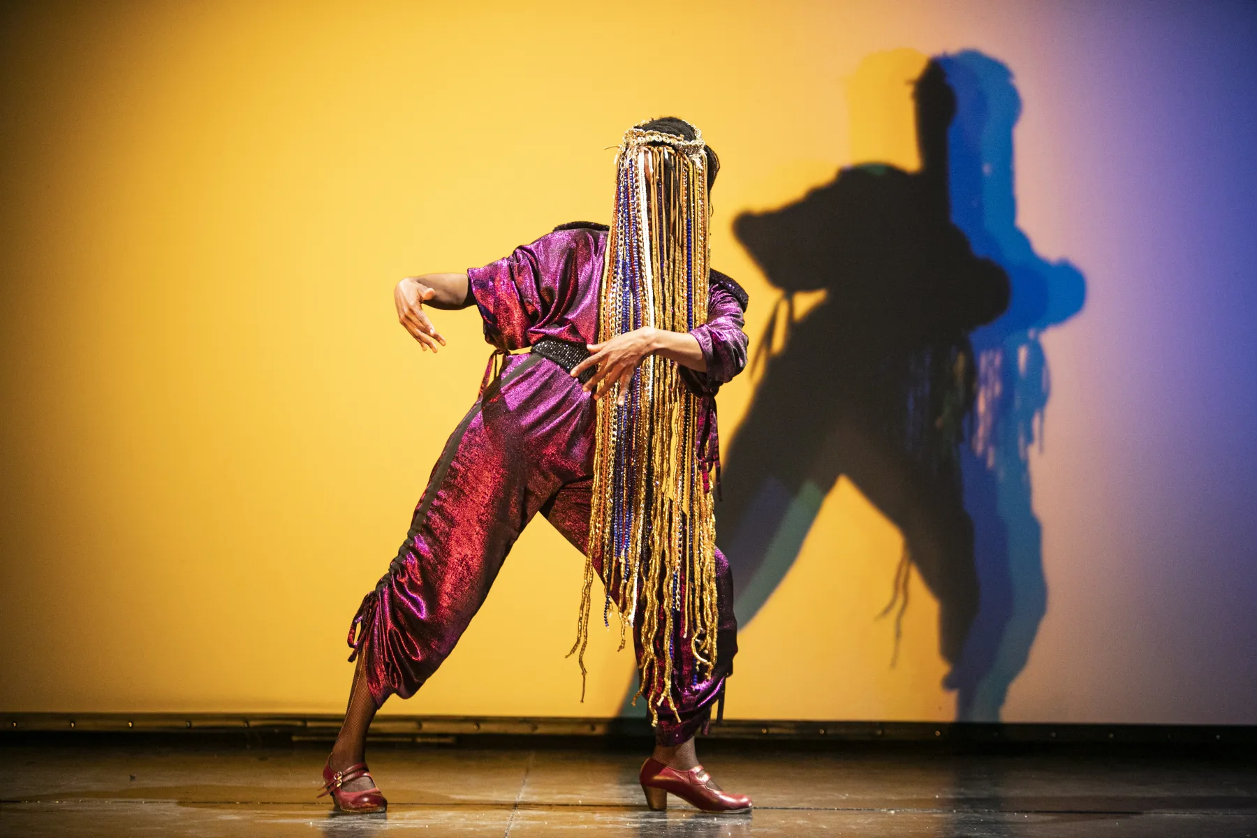 La danseuse, vêtue d'une combinaison rose, danse devant un mur jaune, on ne voit pas son visage