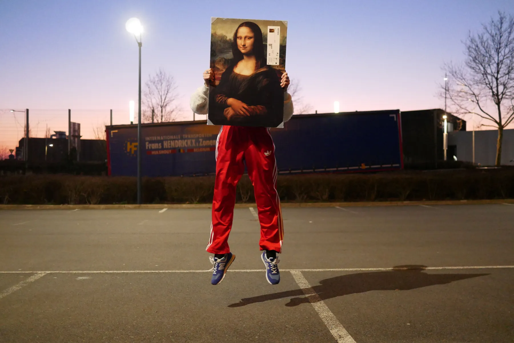 Sur un terrain sportif, une personne saute en l’air, tenant devant elle un tableau de La Joconde